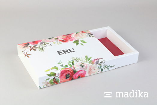 Die Schiebeschachtel mit Hohlwand greift bei der Bedruckung des Einlegers die Farben des Blumenmusters auf. Offene Schiebeschachtel mit Hohlwand und Blumenmuster