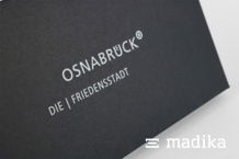 Schwarze Naturkartonschachtel mit hellem Logo. Detail einer schwarzen Naturkartonschachtel mit heller Bedruckung