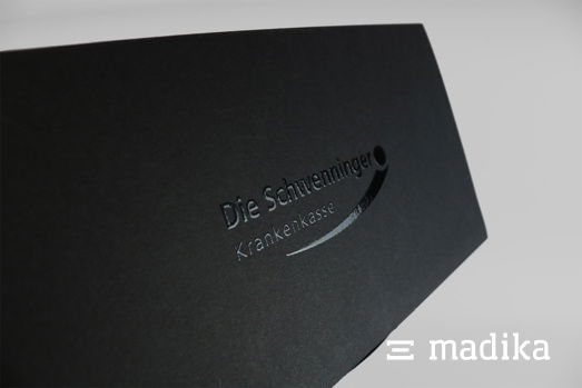 UV-Lackierung in Form des Logos auf schwarzem Karton. UV-Lackierung auf schwarzem Karton