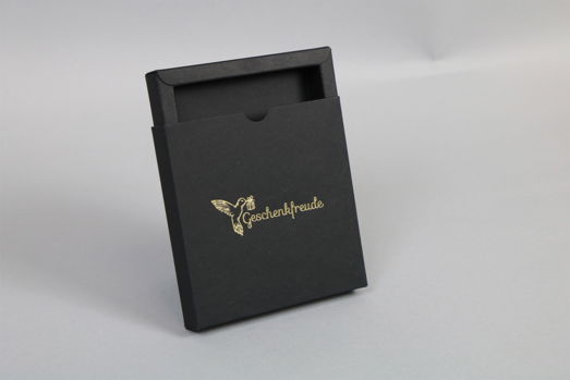Halb offene Schiebeschachtel aus schwarzem Karton mit goldener Heißfolienprägung Halb offene Schiebeschachtel aus schwarzem Karton mit goldener Heißfolienprägung