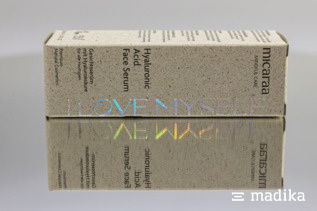 Heißfolie mit Effekt: Der Hologramm-Schimmer kommt dank der Spiegelung schön zur Geltung. Kosmetikverpackung liegt auf der Seite. Eine Spiegelung zeigt die bunten Variationen der Hologramm-Heißfolie.